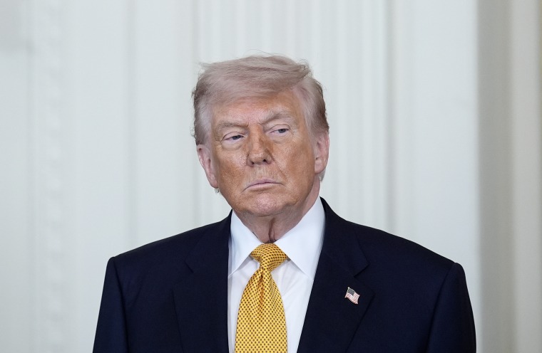 Donald Trump gazes to the side while standing in front of a white wall in the White House.