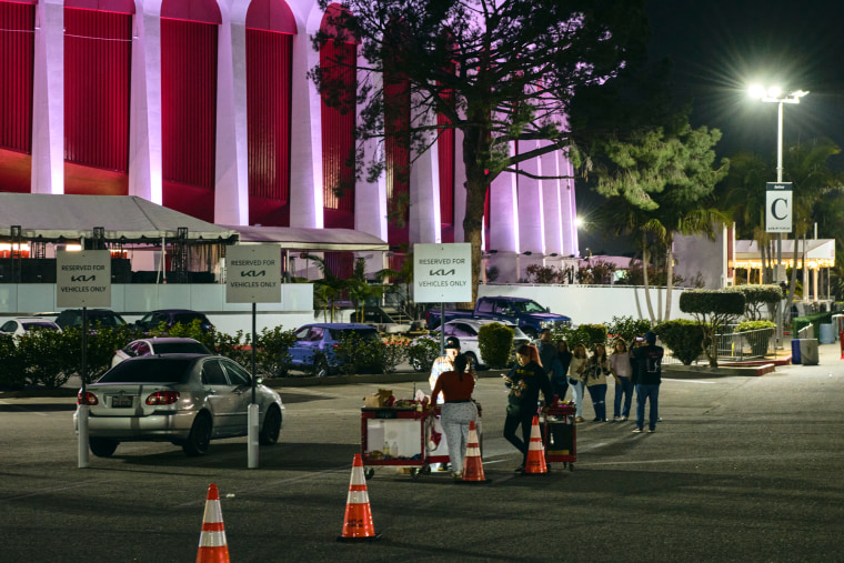 People stand near vendor carts in a parking lot outside of the Kia Forum building