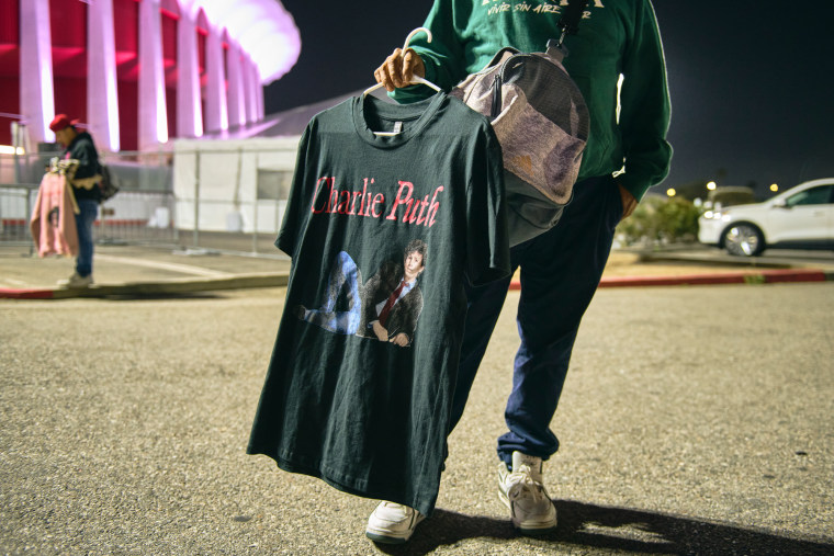 A person holds a Charlie Puth t-shirt in a parking lot
