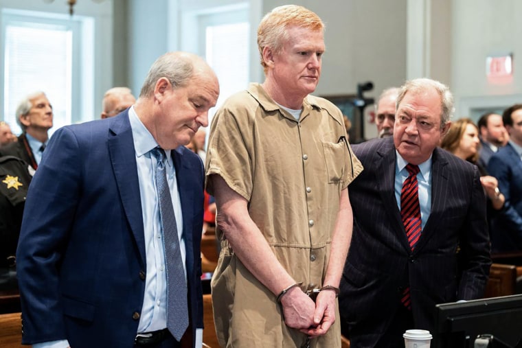 Alex Murdaugh stands handcuffed between two lawyers in a courtroom.