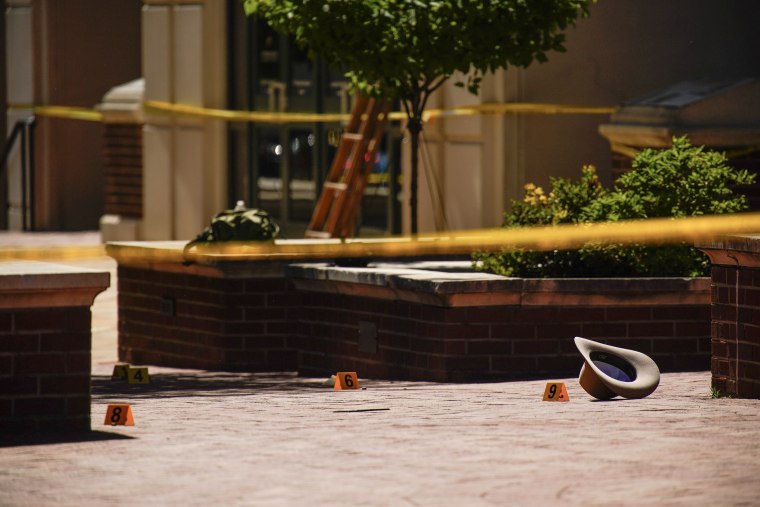 Orange ballistic markers arranged on a brick courtyard next to a cowboy hat, with yellow crime scene tape stretched across the frame.