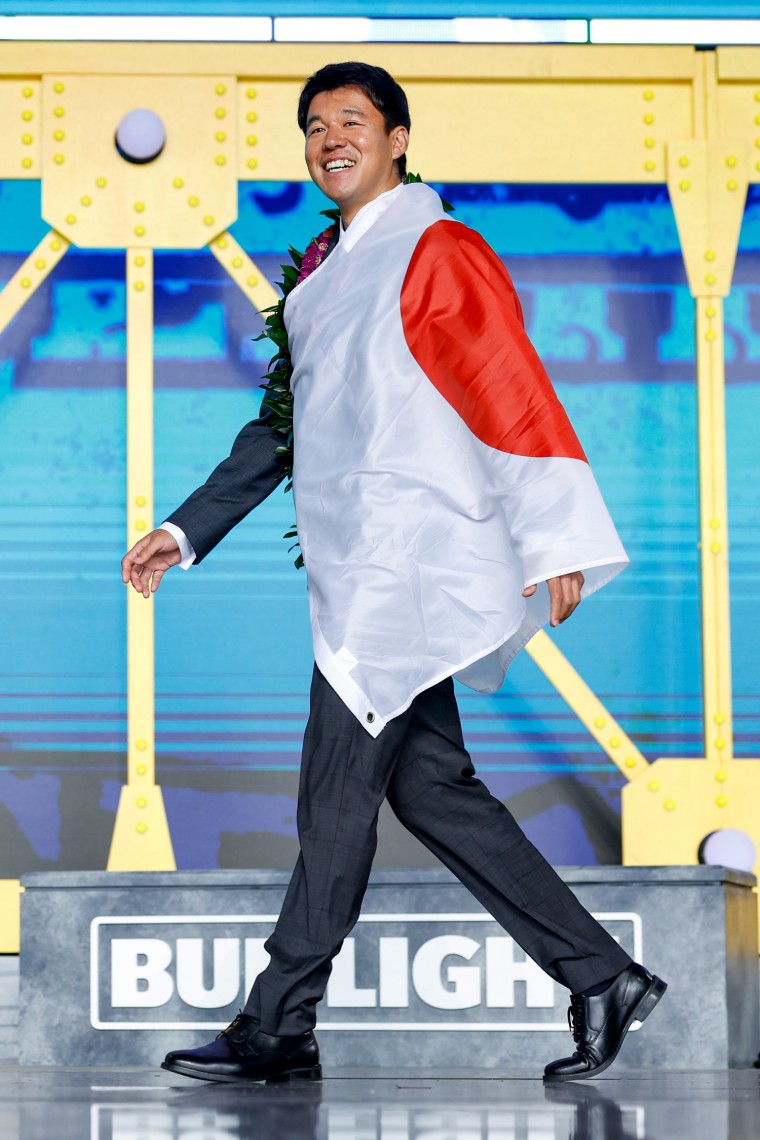 Kansei Matsuzawa walks on stage with a large Japanese flag draped over his shoulder