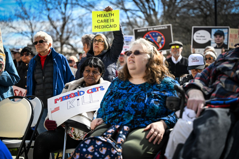 A large crowd of people hold signs against medicaid cuts outside