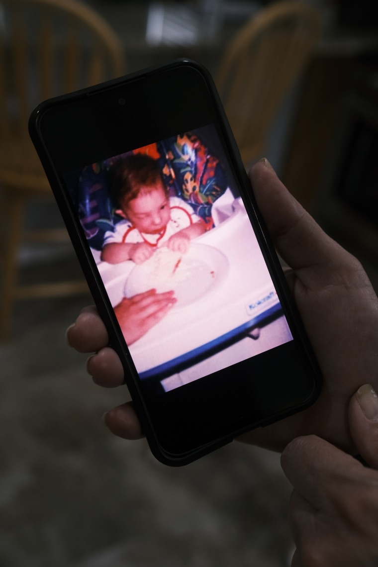 A hand holds up a cellphone displaying a photo of Jason Gonce seated in a baby chair as a baby