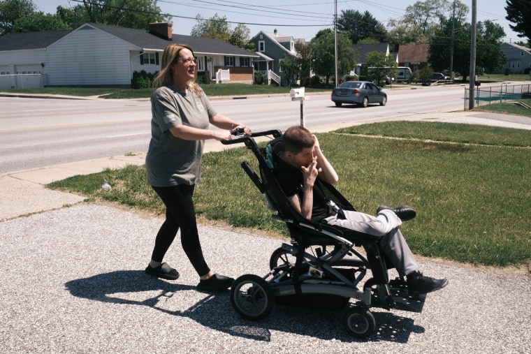 Melissa Gonce wheels her son Jason, in a wheelchair, on a sidewalk outside in a residential area