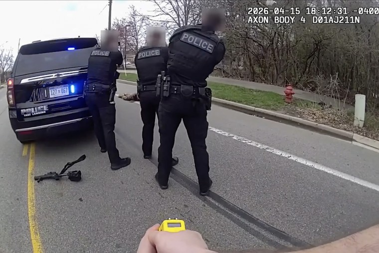 Three police officers face away from the camera and toward a man lying on the ground in front of them. 