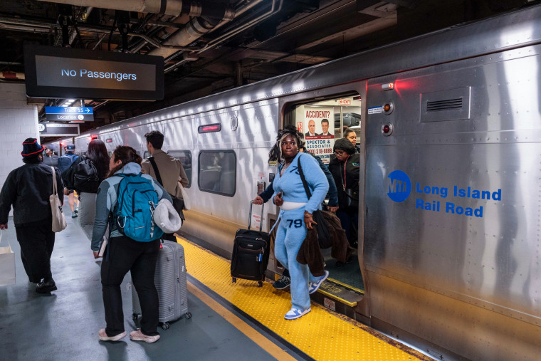 People exit a Long Island Rail Road train cart inside of a station
