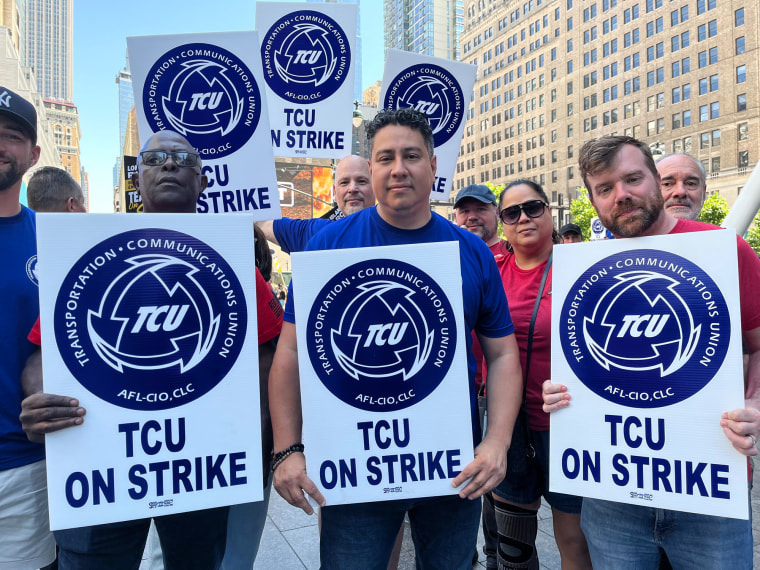 People hold picket signs on the street outside
