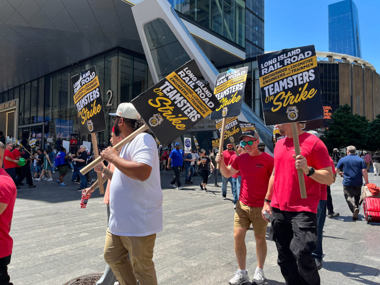 People hold picket signs proclaiming a strike while marching on the street outside