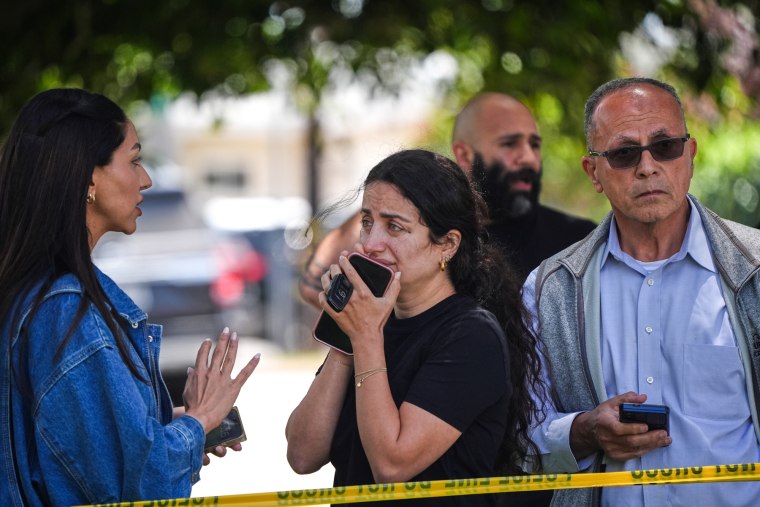 People stand behind police tape at the scene of a shooting