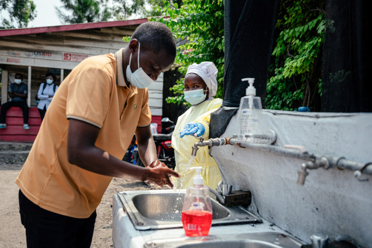 A visitor washes his hands at a sink operated by a hospital worker before entering Kyeshero Hospital 