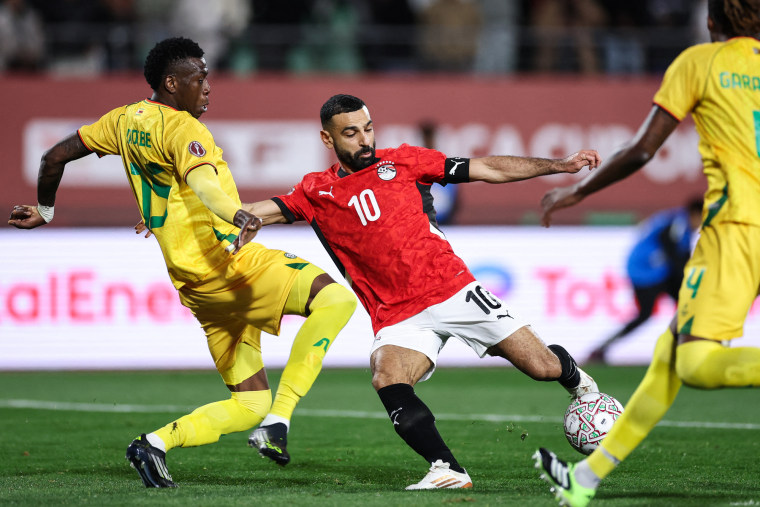 Mo Salah, center, kicks the soccer ball while in between two players from the opposing team