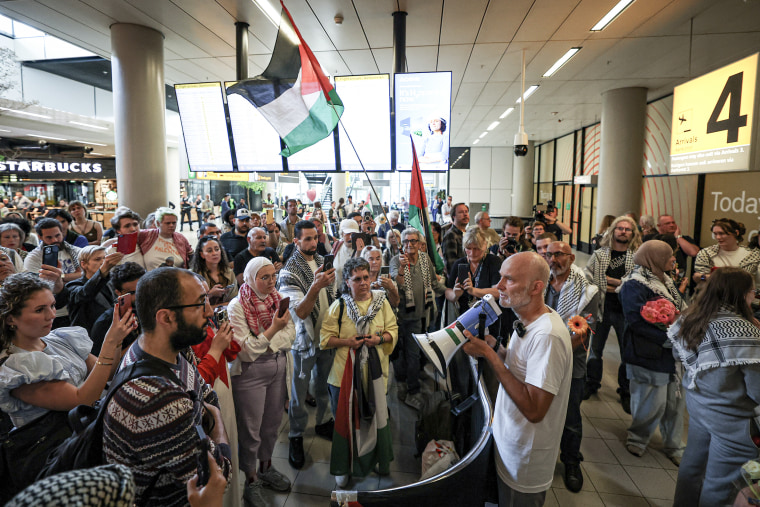 A man with a megaphone standing in front of a crowd of people inside an airport.