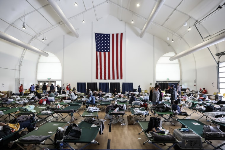 A large american flag hanging on the wall of a makeshift shelter in a large white hangar. 