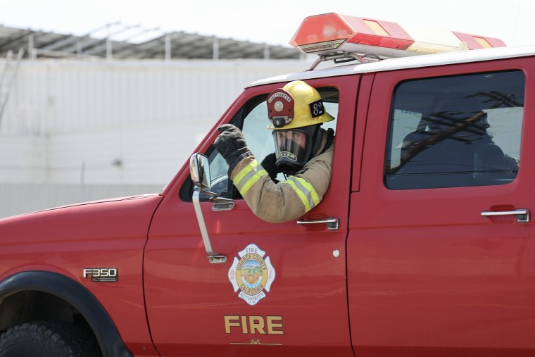 A firefighter in a red truck leans out of the driver's window and points.
