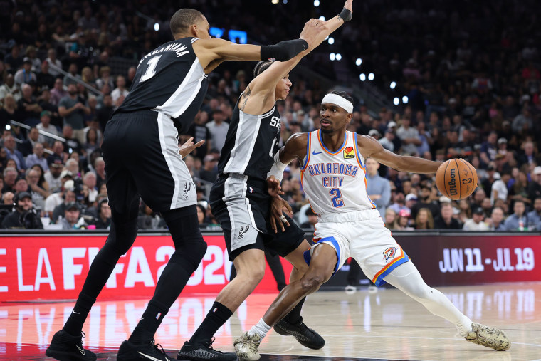 Shai Gilgeous-Alexander of the Oklahoma City Thunder drives around Carter Bryant and Victor Wembanyama of the San Antonio Spurs on May 28, 2026.