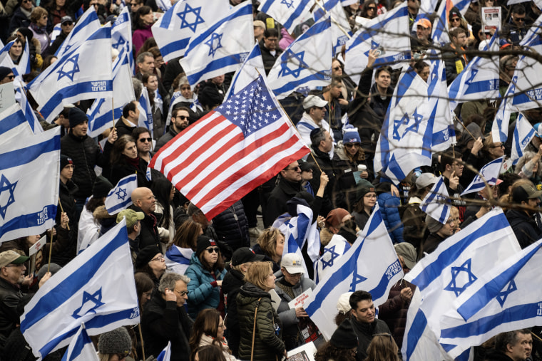 A lone American flag is held among dozens of Israeli flags in a crowd of people.