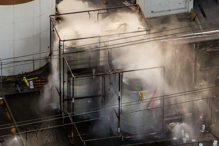 An aerial photo of three large industrial tanks with water being sprayed and misted onto them.