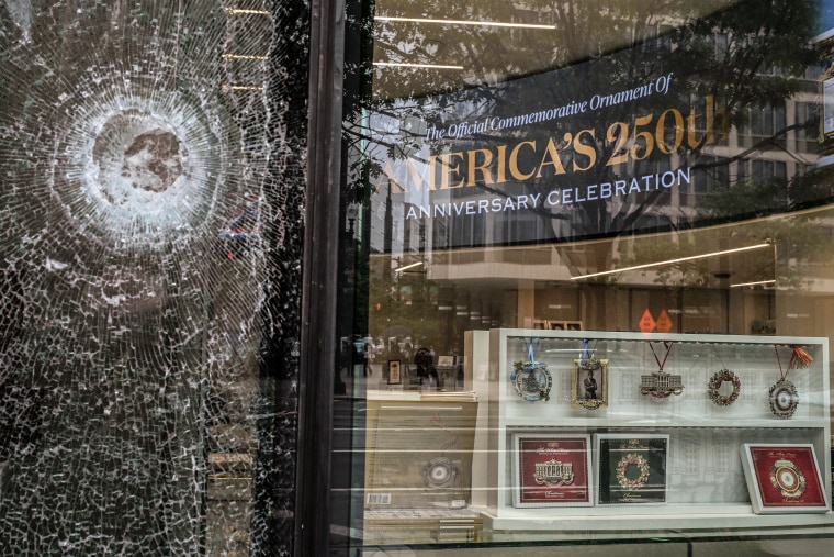 A large bullet hole in a shattered window of a store.
