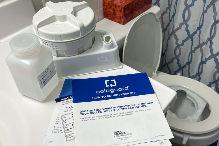 A Cologuard lab kit is seen inside of a bathroom on a sink next to an open toilet