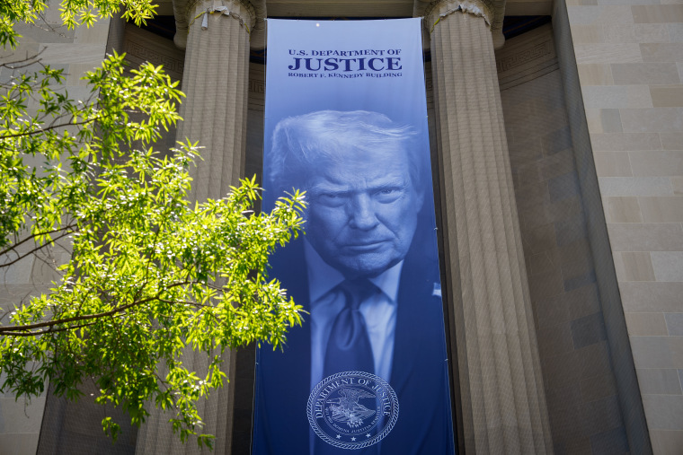A blue banner with Donald Trump's face hanging on the outside of the DOJ headquarters.