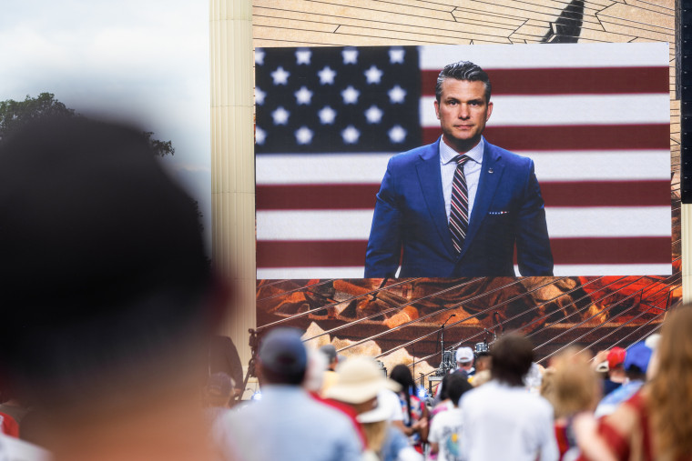 Pete Hegseth appears on a jumbo screen in front of an outdoor audience.