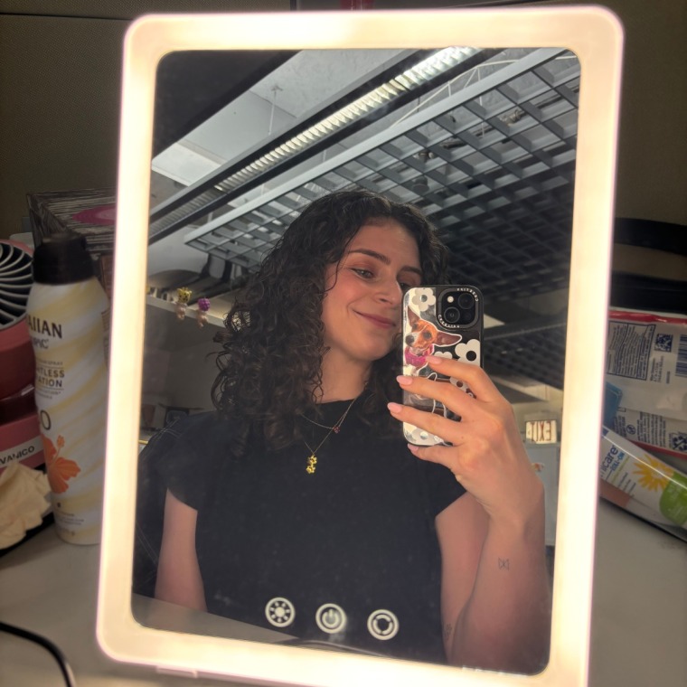 A woman taking a picture of herself in the Ilios Lighting Slim Mirror.