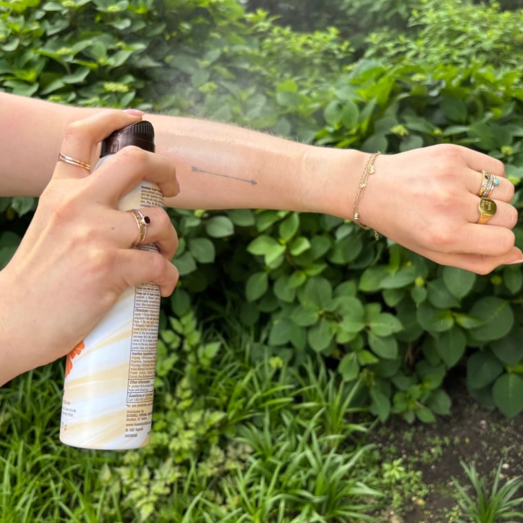 A woman applying Hawaiian Tropic’s Weightless Hydration Clear Spray Sunscreen SPF 30.