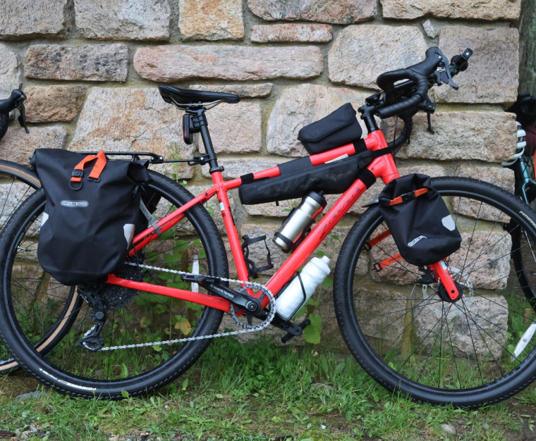 A red bike with bags attached, leaning against a stone wall.