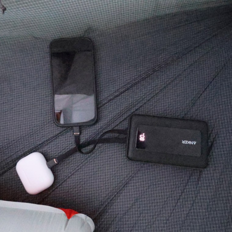 A power bank charging an iPhone and Apple AirPods on the floor of a tent.