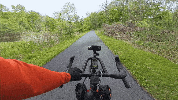 A POV video of someone riding a bike on a paved trailway in the woods.