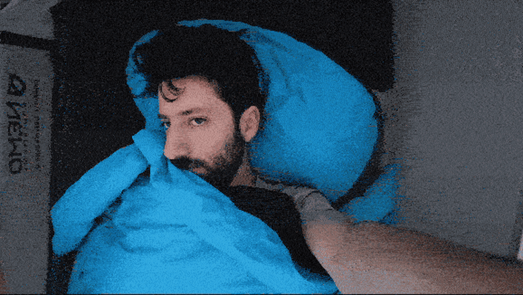 A video of a man laying down inside a tent, pulling his arm out of a sleeping quilt.