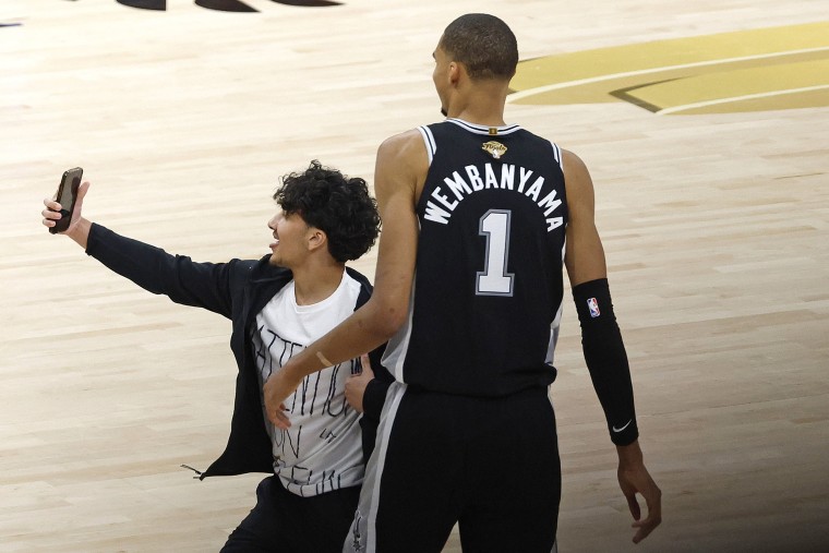 A fan runs onto the court and takes a selfie with Victor Wembanyama of the San Antonio Spurs