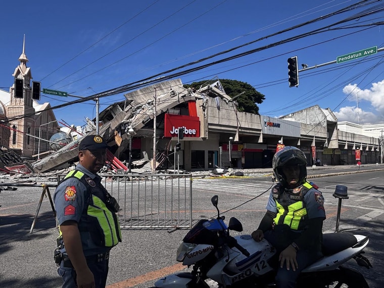 A severely damaged commercial building behind two police officers.