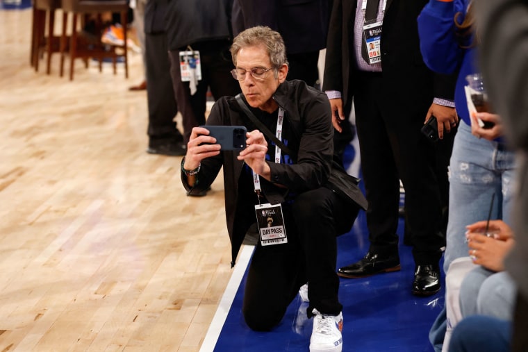Ben Stiller kneels on the court to take photos.