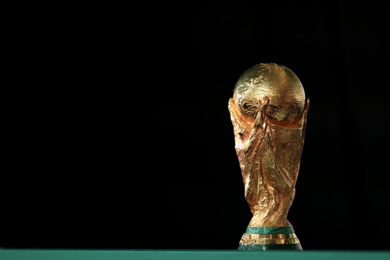The gold world cup trophy is displayed against a black backdrop.