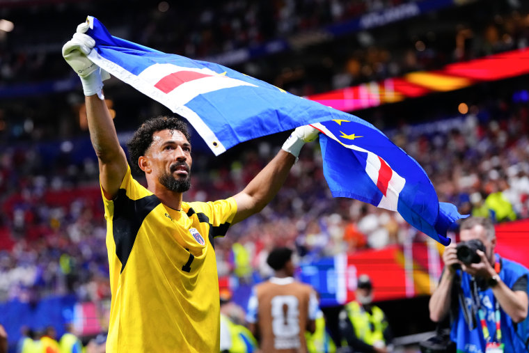 Vozinha raises the Cape Verde flag while standing on the soccer field