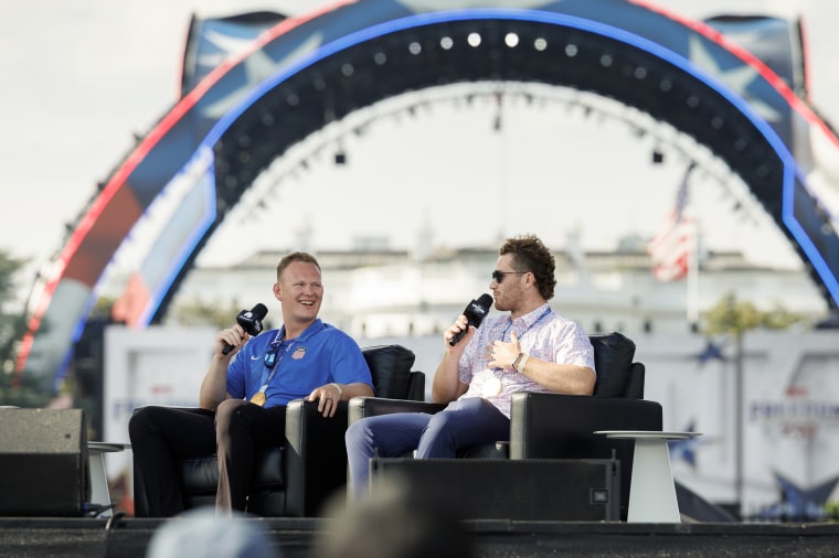 Matthew Tkachuk and Brady Tkachuk sit in black chairs holding microphones on an outdoor stage.
