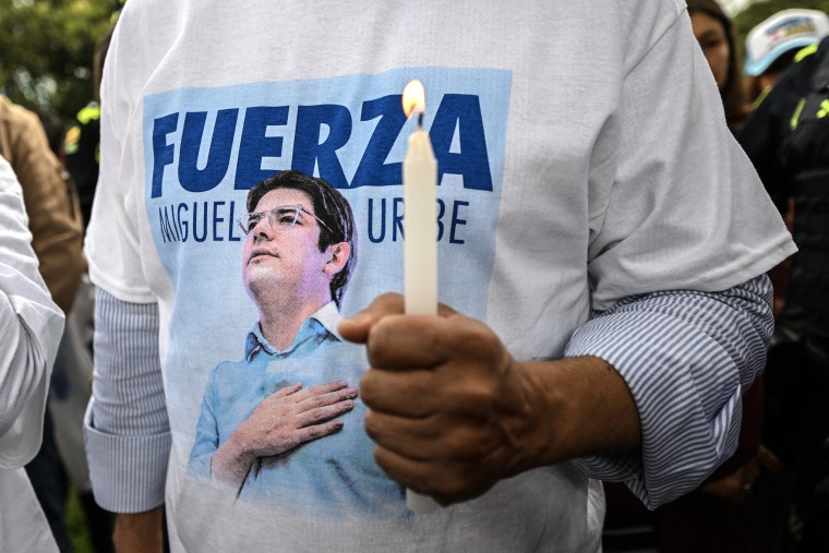 A man wearing a memorial t-shirt with Miguel Uribe on it holds a candle.