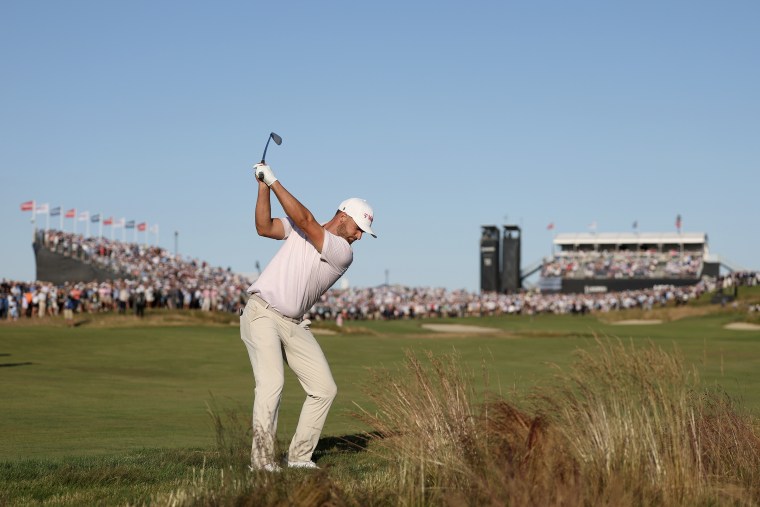 Wyndham Clark swinging a golf club in front of a distant crowd.