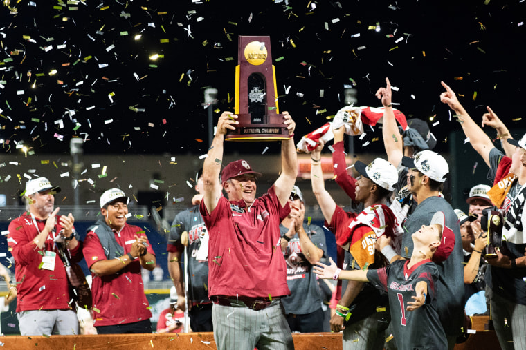 Oklahoma Sooners head coach Skip Johnson holds up the championship trophy next to players on the field as confetti falls