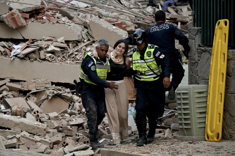 Emergency responders helping an injured woman from a damaged building.