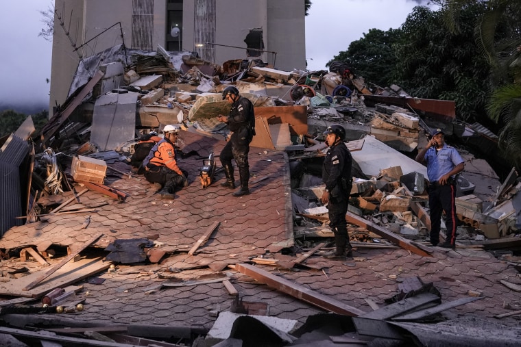 Emergency responders stand on top of a collapsed building.