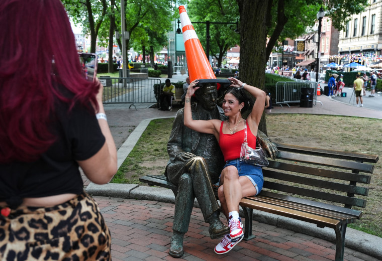 A woman poses next to a statue wearing a traffic cone for a photo her friend is taking