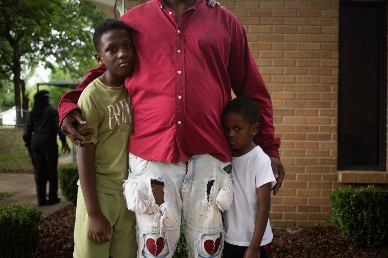 A man, seen from the neck down, with his arms around his two sons.