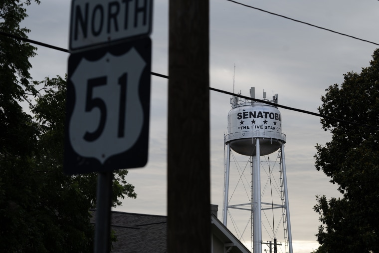 A steel water tower appears behind a highway road sign at dusk.