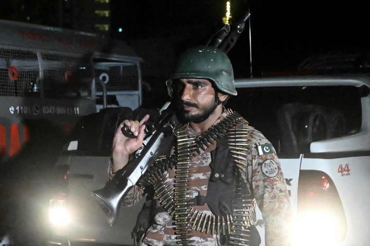 An armed soldier illuminated by headlights at night.