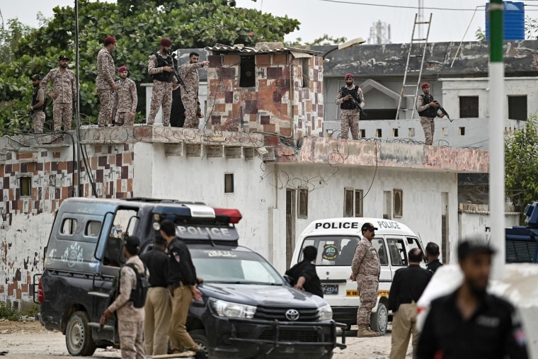 Soldiers standing atop a low concrete building with a police van parked below.