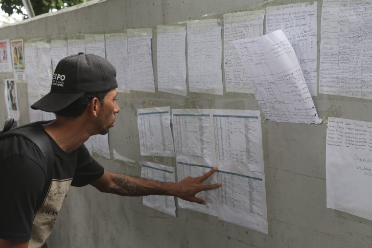 A man looking at lists of names posted on a wall.