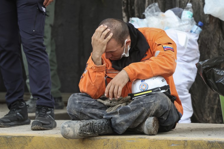 A rescue worker sits on the ground with his head in his hands.